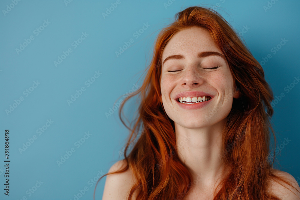 A smiling redhead woman with closed eyes savoring a peaceful moment against a serene blue background, embodying bliss and contentment.