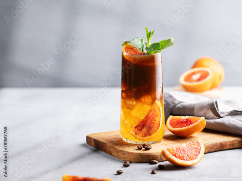 Coffee with orange juice (bumble) in a tall glass with ice and mint on a wooden board on a light background
