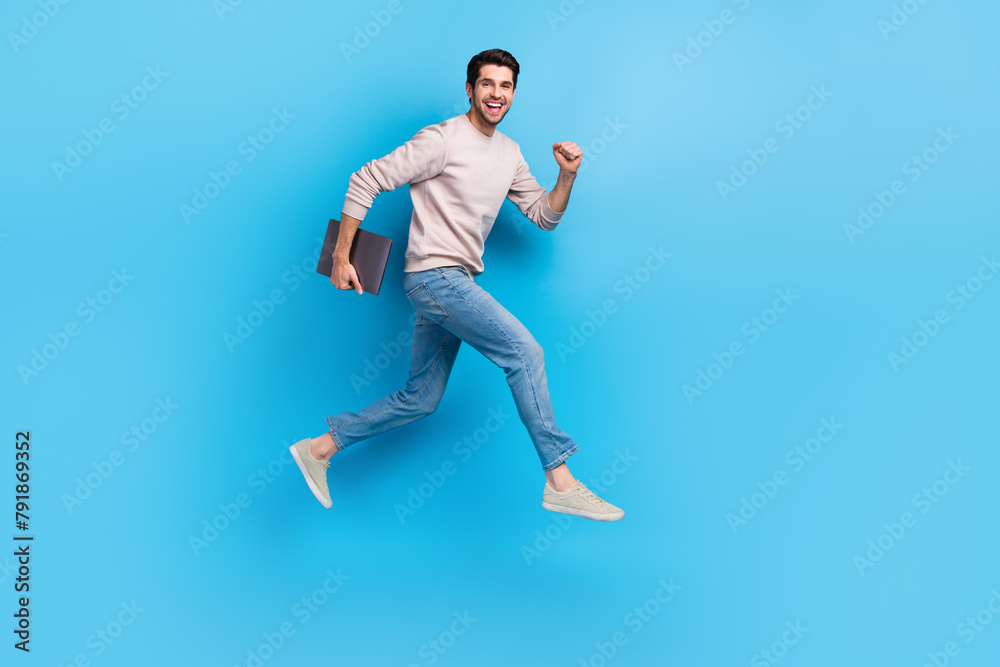 Full size photo of optimistic cheerful man wear sweatshirt denim pants run to empty space with laptop isolated on blue color background Full size photo of optimistic cheerful man wear sweatshirt denim pants run to empty space with laptop isolated on blue color background