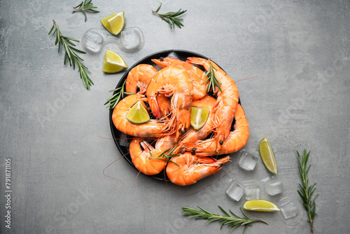 Fresh shrimps with ice, lime and rosemary on grey background, top view