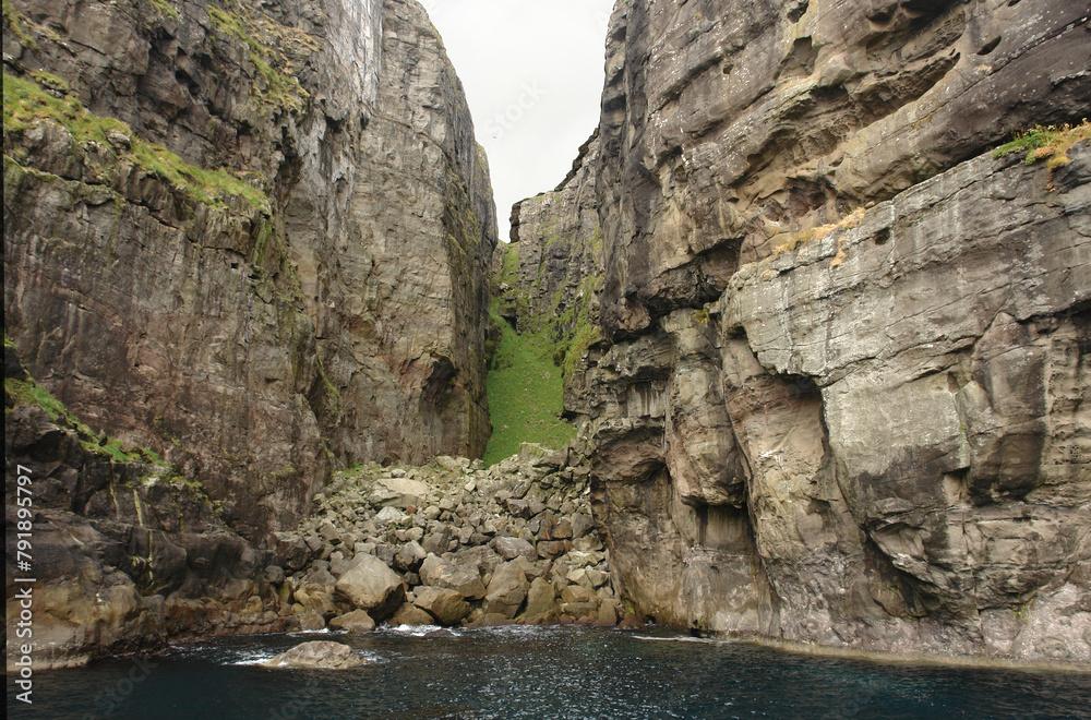 Rocks and caves of the coast near the famous spireTrøllkonufingur  towering rock formation on Vágar Island