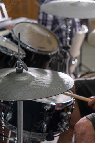 Close-up of a man's hands playing drums. His drumsticks hit with energy, showing the rhythm and motion of live performance. Cymbals and drumheads are slightly blurred, indicating movement.