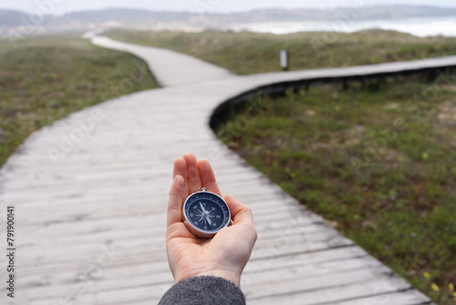 A person holding a compass on a wooden boardwalk. The promenade has two paths.
