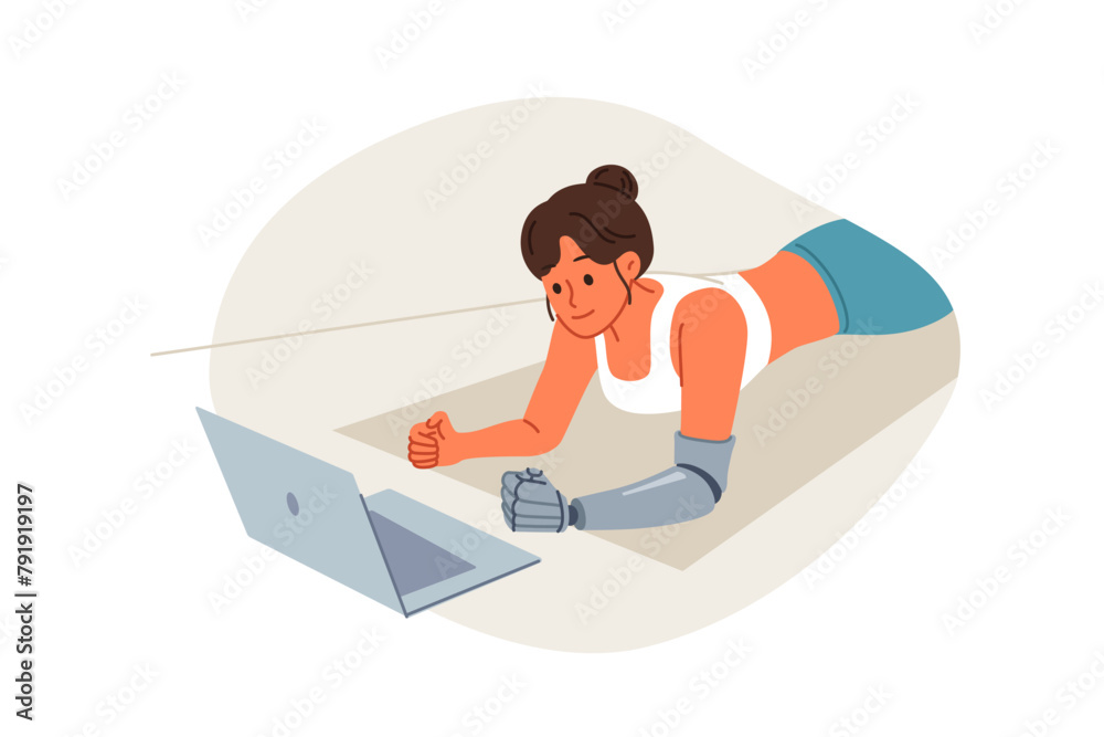 Sports woman with prosthetic arm trains at home and watches video lesson on laptop, lying on floor in plank. Sports girl doing yoga on fitness mat, training to improve health and muscle development