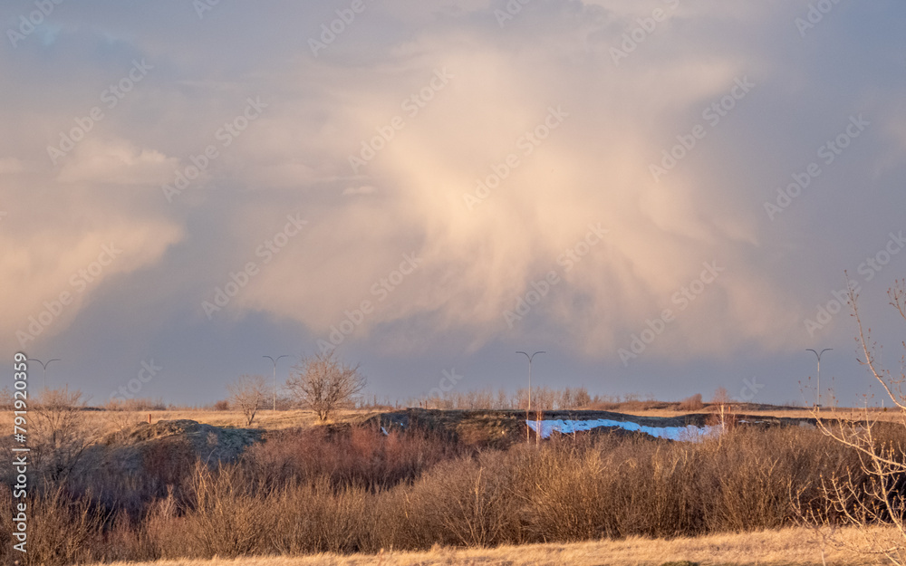 Evening fluffy clouds over Crocus Prairie Park in Saskatoon with spring snow leftovers