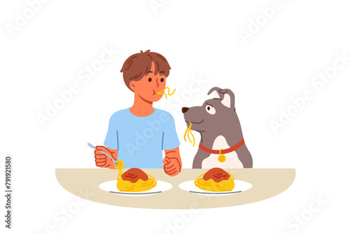 Little boy and dog eat spaghetti sitting at table, demonstrating friendship and trust. Child lives in harmony with dog, teaching puppy to accept food from plate and enjoying communication with pet