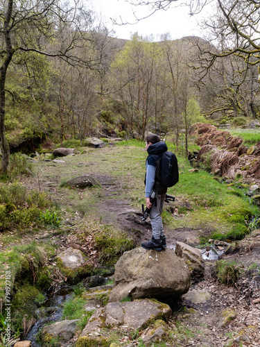 Young photographer standing on a large rock in a forest woodland scene with a slow moving moorland stream surrounded by trees