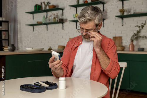 Middle aged man with glucometer checking blood sugar level at home photo