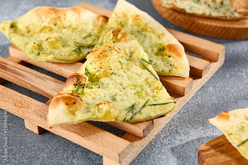 Focaccia with rosemary on a wooden serving board, highlighted by natural sunlight and textured gray background