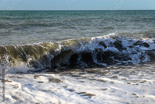 A soft sea wave on a sandy beach. Close-up of a wave on the Black Sea coast. Sea foam of a coastal wave on a sandy beach in close-up. Coastal waves. Selective focus.