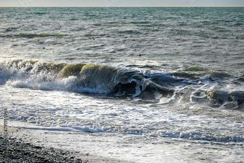 Close-up of a wave on the Black Sea coast. A soft sea wave on a sandy beach. Sea foam of a coastal wave on a sandy beach in close-up. Coastal waves. Selective focus.