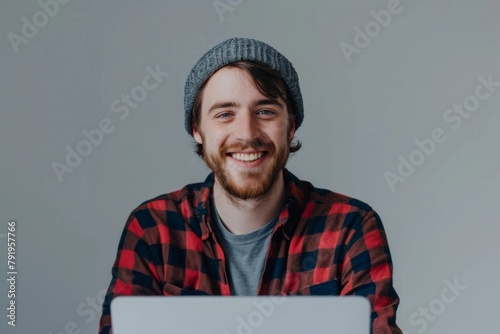 A young cheerful man in a beanie is smiling while working or surfing on his laptop computer