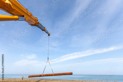 Crane carrying steel piles to coast for new pier installation. 