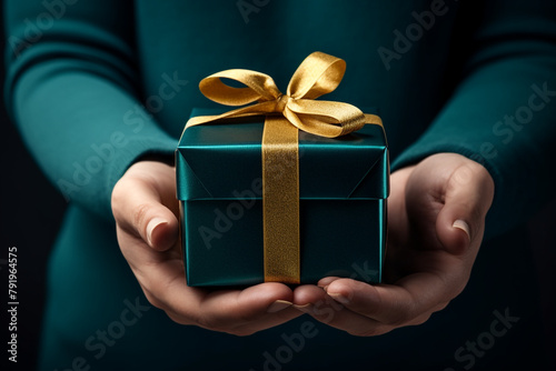 hand holding a present box with gold bow on dark background, in the style of dark teal and dark indigo сreated with Generative Ai © Andrii Yablonskyi