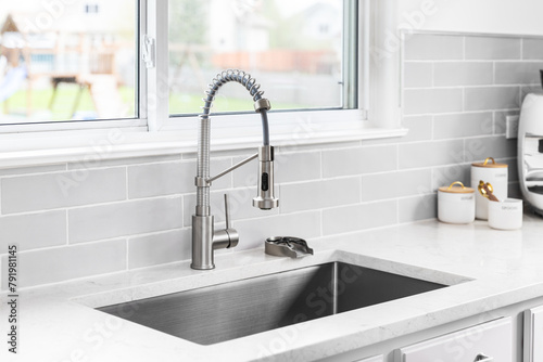 A kitchen faucet detail with a stainless faucet and sink, grey subway tile backsplash, and decorations on the marble countertop.