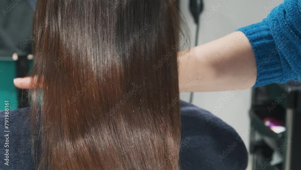 Demonstration of smooth and silky brunette hair after straightening and keratin treatment. Hairdresser shows a lock of shiny and silky brunette hair after straightening in beauty salon