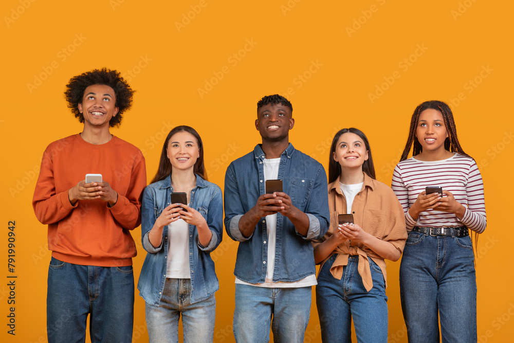 Fototapeta premium Engaged young people using mobile technology on orange background