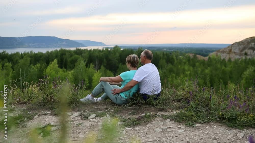 elderly couple sitting on a mountain admires the landscape at sunset. Senior couple walking in nature. travel tourism concept. spends time in nature in summer. elderly couple sitting on a mountain admires the landscape at sunset. Senior couple walking in nature. travel tourism concept. spends time in nature in summer.