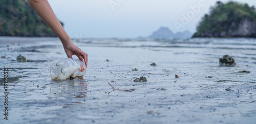 Woman hands pick up plastic pet bottle left on the beach, Cleaning the beach, Collecting trash at the beach. Environmental Conservation concept. © surasak