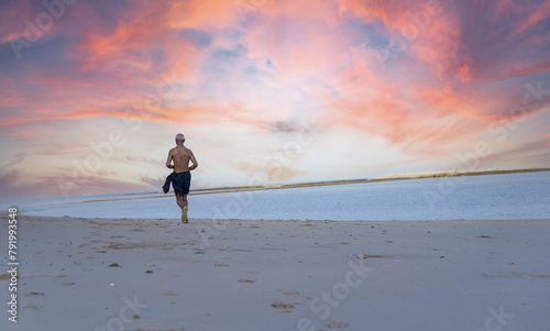 Older man with fit strong body  in sports clothes warm up training run jogging on the beach next to the sea at sunset on summer beach sand, running in sport well being and healthy lifestyle concept.