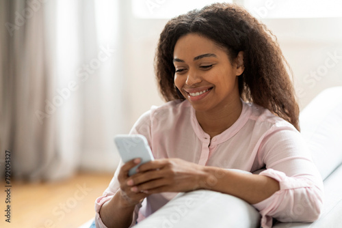 Content woman browsing phone while relaxing at home