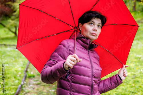 A girl in the rain in a purple jacket with an umbrella looks at the sky.