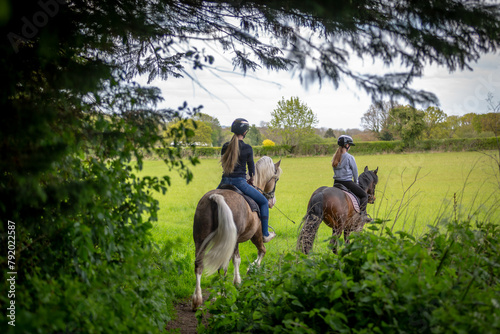 Obraz na płótnie Two young girls horse riding across a field, Image shows the rear view of 2 girl