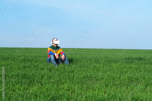 Man sitting on green grass in virtual reality glasses of the blue sky on the background, low viewing angle. Sustainable agriculture. outdoors. space for text