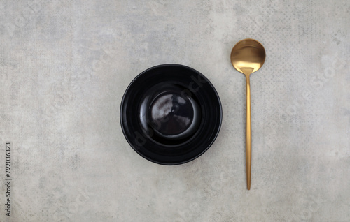Empty black plate, gold metallic spoon on marble rustic concrete background. Top view, flat lay.