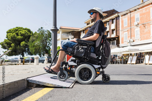 Male tourist on wheelchair crossing over the threshold ramp on the seaside promenade. Disability and accessible tourism concepts.