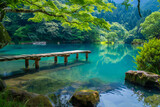 A beautiful lake with a wooden bridge leading to it. The water is calm and clear, reflecting the surrounding trees and sky. The scene is peaceful and serene, inviting visitors to relax
