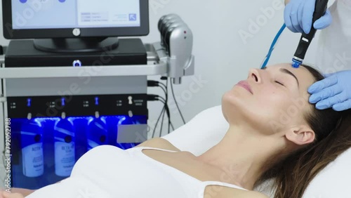 Beautician in gloves conducts vacuum cleaning and polishing face skin of young woman in cosmetology clinic. Professional moisturizing and rejuvenating hardware procedures for modern people.