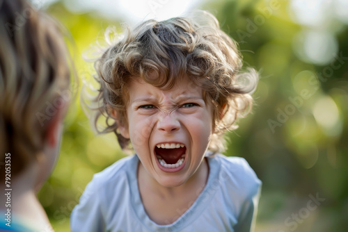 A young boy is crying and has his mouth open. He is surrounded by trees and grass. Scene is sad and emotional