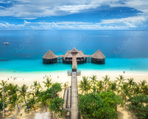 Aerial view of bungalow, white sandy beach, ocean on summer sunny day. Restaurant on the sea. Top drone view of wooden hotel, azure water, palms, sky with slouds. Luxury resort in Kendwa, Zanzibar