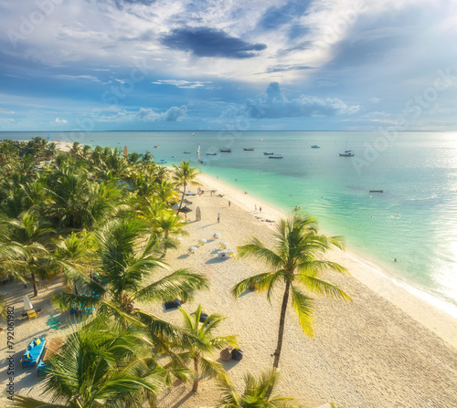 Aerial view of sandy beach with palm trees, umbrellas, boats, sea