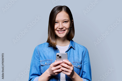 Young smiling woman using smartphone looking at camera in gray background