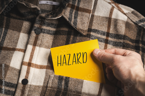 Yellow card with a handwritten inscription "Hazard", held in the hand against the background of a brown plaid shirt (selective focus), translation: gambling