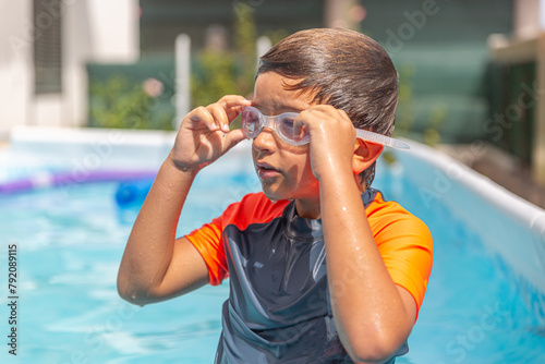 Pensive young boy with swim goggles looks away in a backyard pool. photo