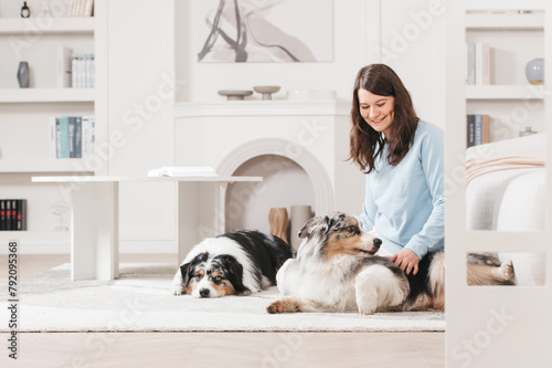 A young woman with two dogs, she sits on the floor in the room and smiles while communicating with her pets. Bright interior. Breed Australian Shepherd Aussie.