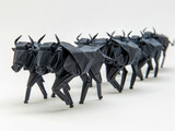 A lineup of origami wildebeest in a migratory herd formation on a white background.
