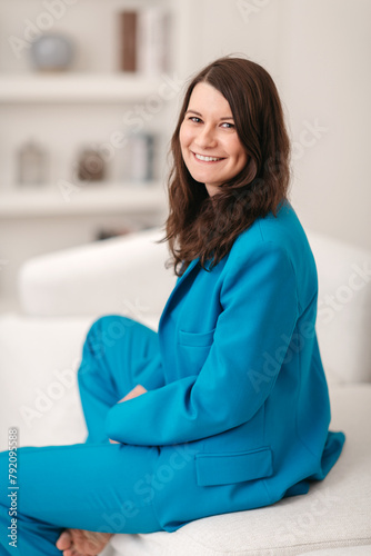 Beautiful happy woman smiling. She is sitting in the interior in a blue business suit. Vertical frame.