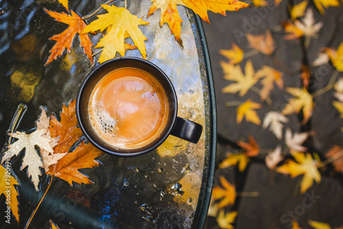Cup of coffee on the patio table, with yellow leaves around, view from the top