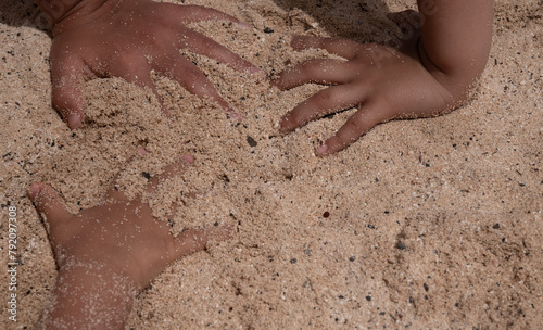 Two hands are in the sand, one of which is slightly higher than the other. The sand is a light brown color and the hands are covered in it