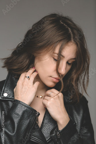 Portrait of a stylish and fashionable woman with a beautiful haircut. Close-up. She looks natural, wearing a black leather jacket. The gaze is directed to the side and the hands are at the neck.