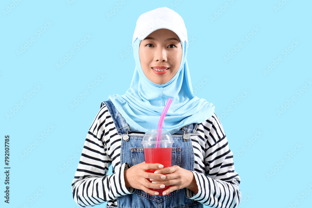 Beautiful young Asian woman in hijab with cup of tasty lemonade on blue background Beautiful young Asian woman in hijab with cup of tasty lemonade on blue background