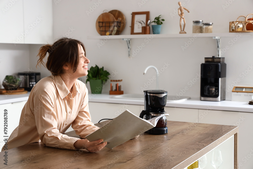Pretty young woman reading magazine in modern kitchen Pretty young woman reading magazine in modern kitchen