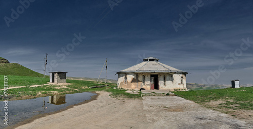 The panorama of an abandoned house against the backdrop of a blue sky and green hills