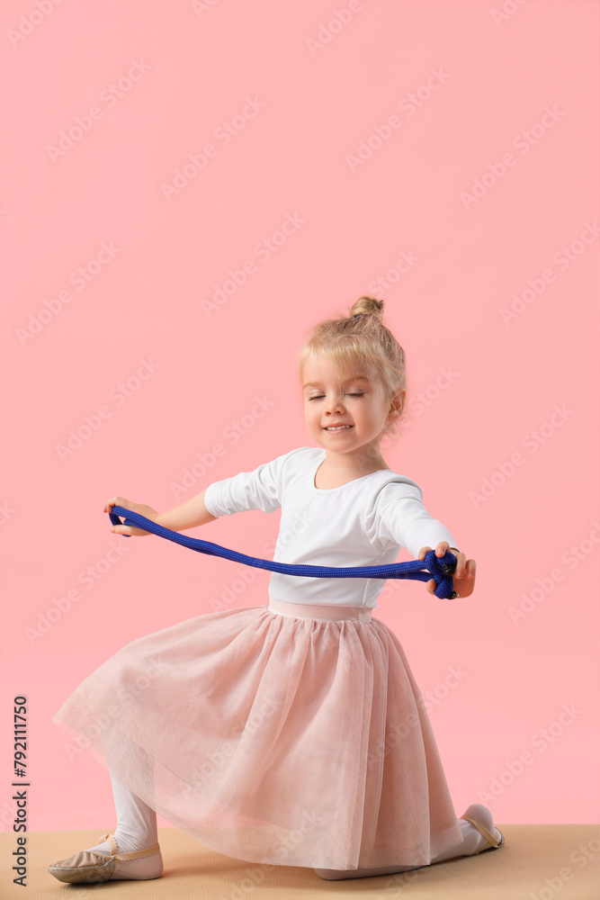 Cute little girl doing gymnastics with rope on mat against pink background Cute little girl doing gymnastics with rope on mat against pink background