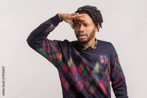 Fotografie Portrait of serious attentive handsome african-american man with dreadlocks and beard keeps hand near forehead, looking far with interest