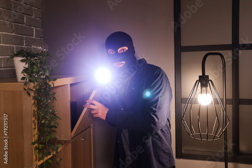 Male thief with flashlight looking for money in room at night
